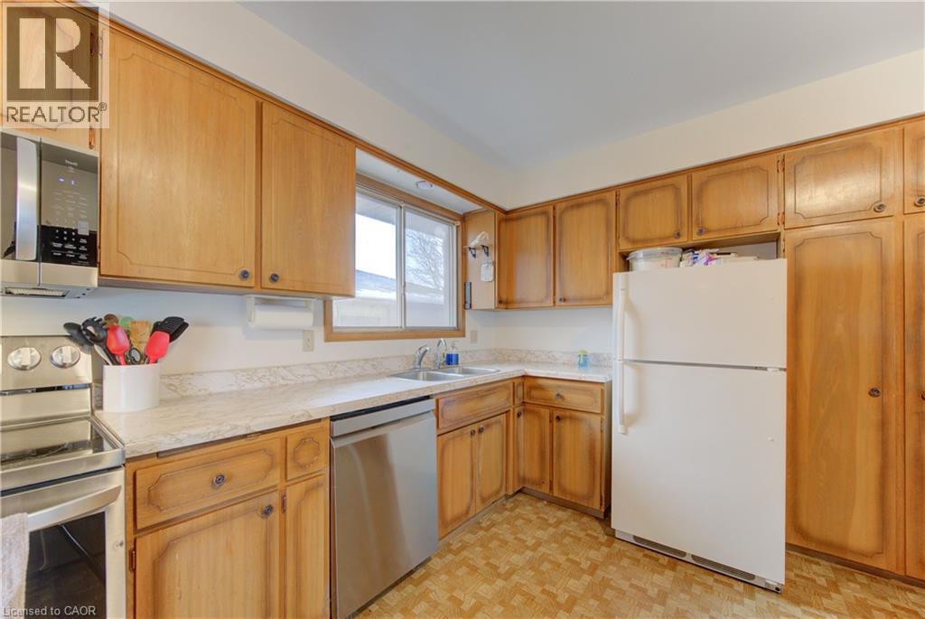 Kitchen featuring extensive wood cabinetry, light-toned countertops, a stainless steel dishwasher, and a window above the sink - 98 Shea Crescent, Kitchener, ON - Indoor Photo Showing Kitchen With Double Sink