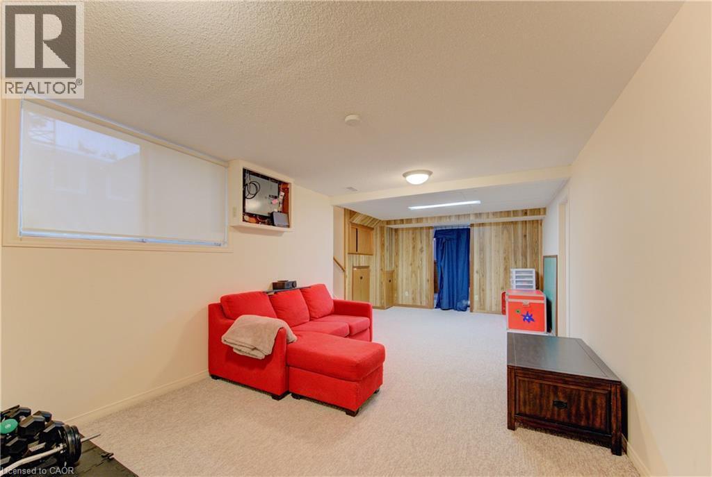 Finished lower level featuring light-toned carpeting, a horizontal window with roller shade, recessed wall niche, a built-in wood-paneled wall with cabinetry, and an overhead light fixture - 98 Shea Crescent, Kitchener, ON - Indoor Photo Showing Other Room