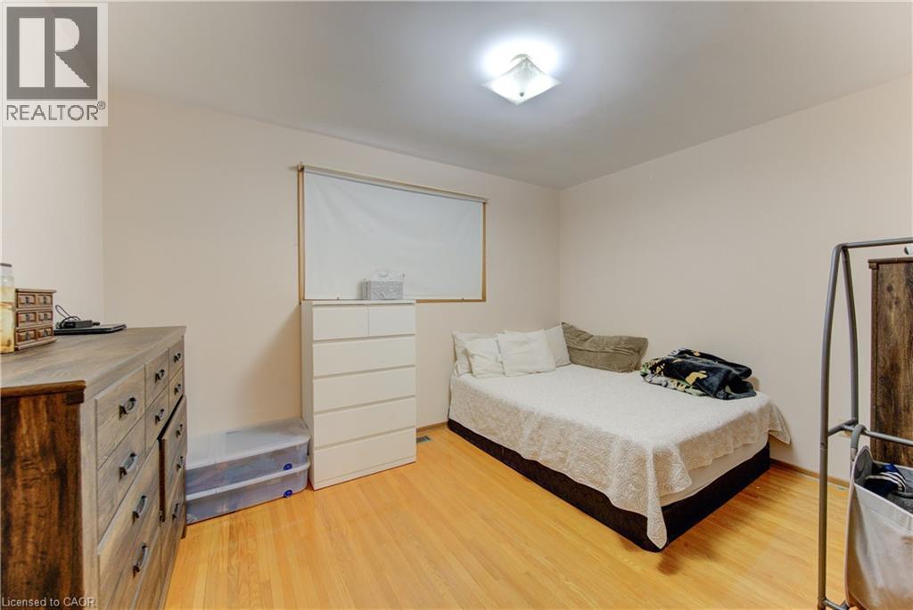 Light-filled room featuring wood-finish flooring, neutral wall tones, a ceiling-mounted light fixture, and a window with a roller shade - 98 Shea Crescent, Kitchener, ON - Indoor Photo Showing Bedroom