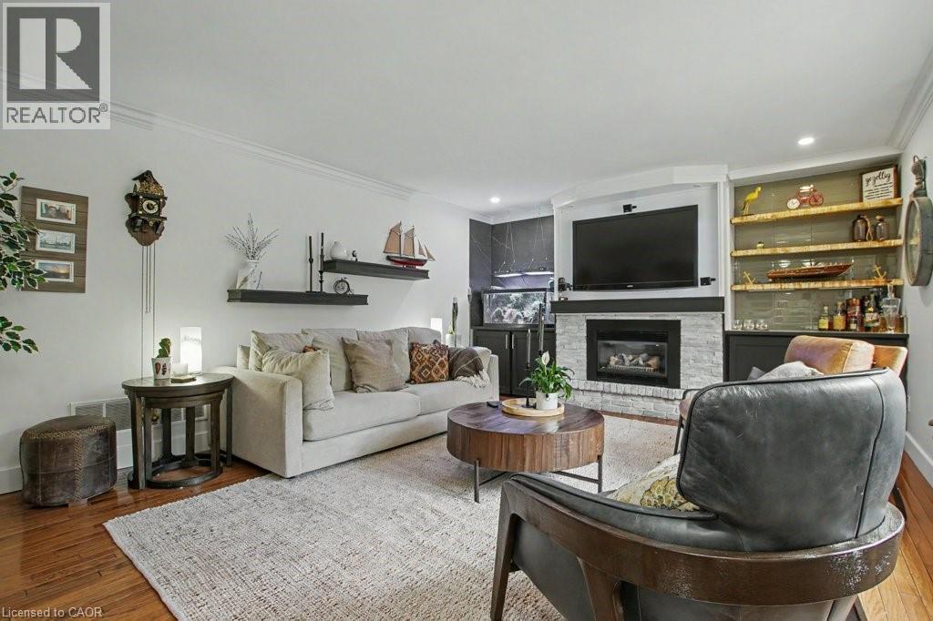 Living area featuring wood-finish flooring, a white brick fireplace with a dark mantel, built-in shelving with recessed lighting, and crown molding - 2324 Homer Drive, Burlington, ON - Indoor Photo Showing Living Room