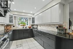 U-shaped kitchen featuring two-tone cabinetry, dark countertops, and a full tile backsplash -