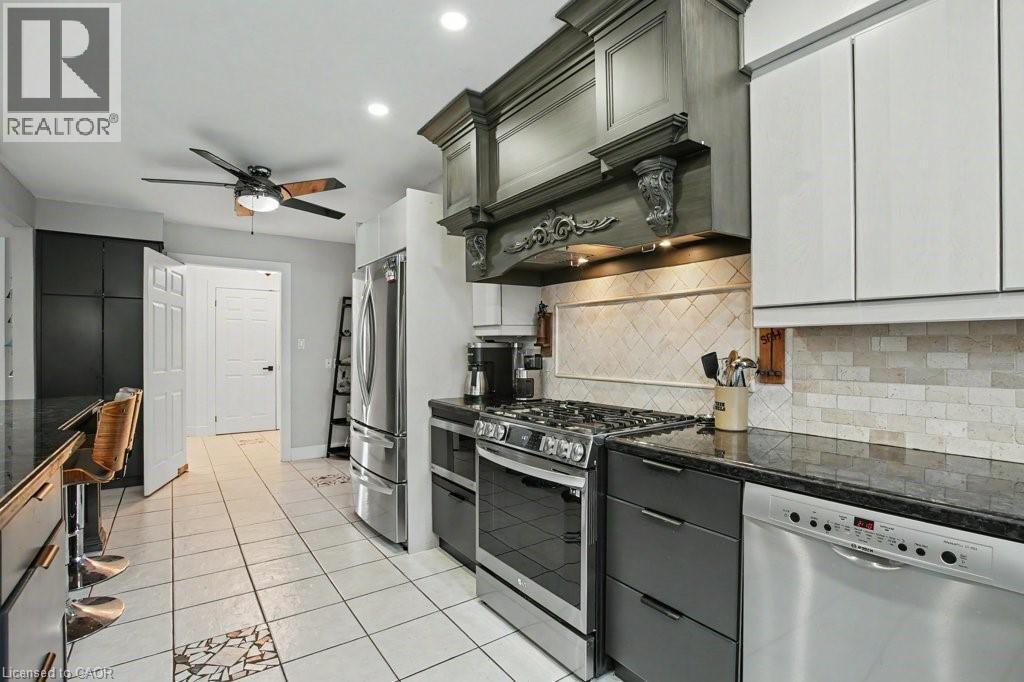 Modern kitchen with white tile flooring, dark granite countertops, and stainless steel appliances - 2324 Homer Drive, Burlington, ON - Indoor Photo Showing Kitchen With Upgraded Kitchen