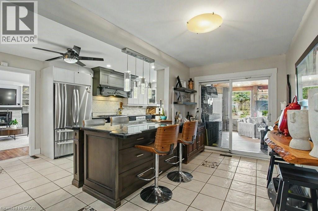 Spacious kitchen featuring an island with seating, stainless steel appliances, tile flooring, and a sliding glass door to an outdoor area - 2324 Homer Drive, Burlington, ON - Outdoor With Deck Patio Veranda