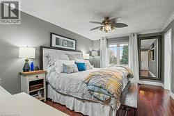 Bedroom featuring crown molding, dark wood-finish flooring, a ceiling fan with integrated lighting, a window with white trim, and a built-in full-length mirror -