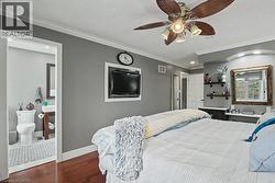 Bedroom featuring wood-finish flooring, a ceiling fan with integrated lighting, and crown molding -