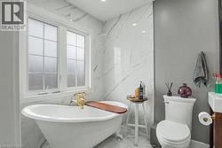 Freestanding porcelain bathtub with ornate gold-finish fixtures, complemented by white grid-patterned windows -