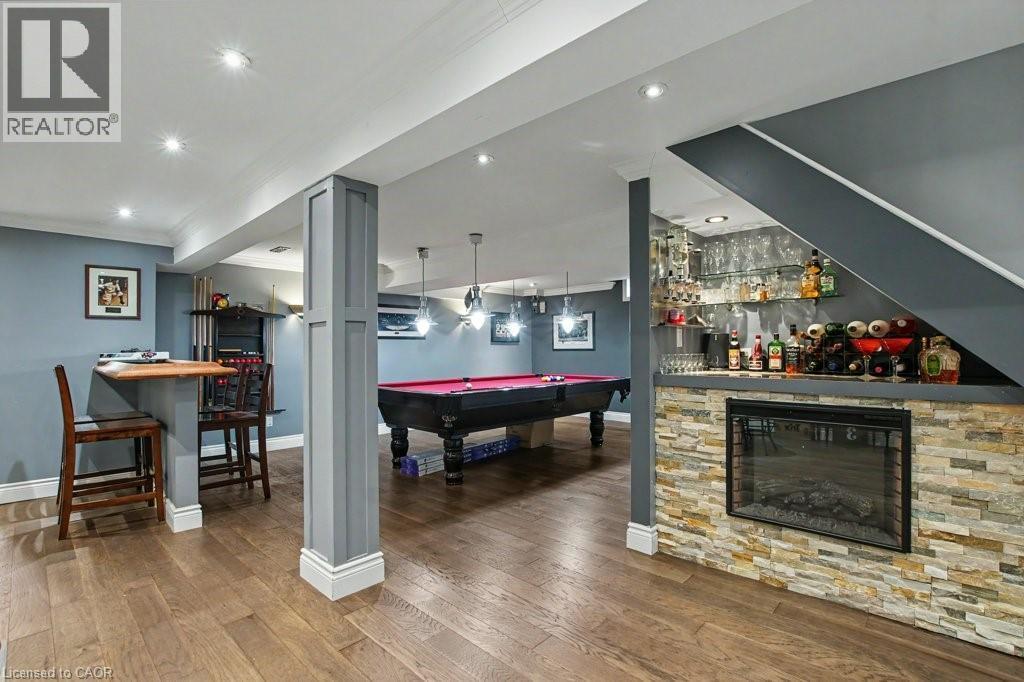 Finished basement featuring wood-finish flooring, recessed lighting, a stone-clad built-in fireplace, and a dedicated bar area with glass shelving - 2324 Homer Drive, Burlington, ON - Indoor Photo Showing Other Room