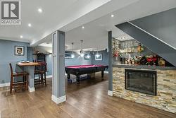 Finished basement featuring wood-finish flooring, recessed lighting, a stone-clad built-in fireplace, and a dedicated bar area with glass shelving -