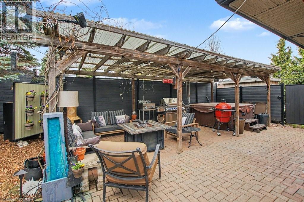 Expansive paver patio featuring a hot tub, a built-in pergola with a clear corrugated roof, and perimeter fencing - 2324 Homer Drive, Burlington, ON - Outdoor With In Ground Pool