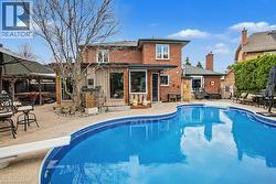 Spacious backyard featuring a large swimming pool with diving board, extensive paver patio, brick exterior, and a covered outdoor entertainment area -