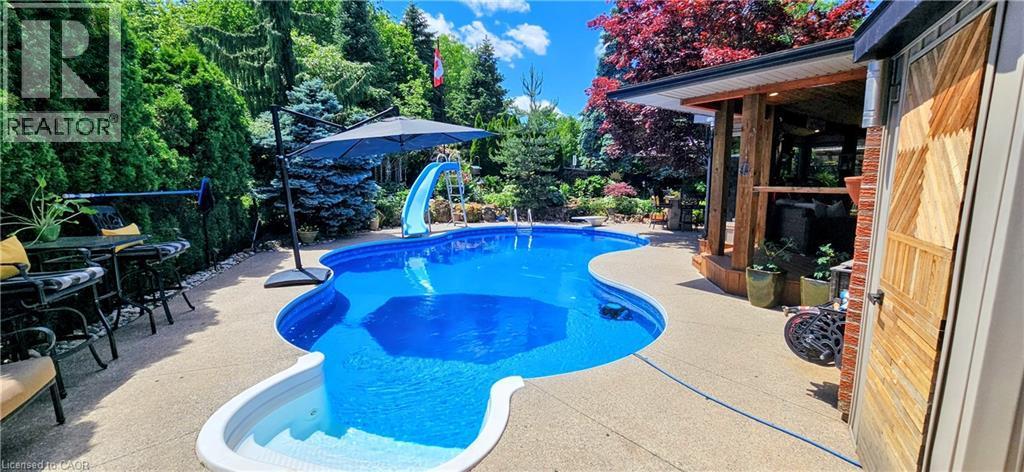 Freeform swimming pool with integrated steps, surrounded by a concrete patio - 2324 Homer Drive, Burlington, ON - Outdoor With In Ground Pool With Backyard