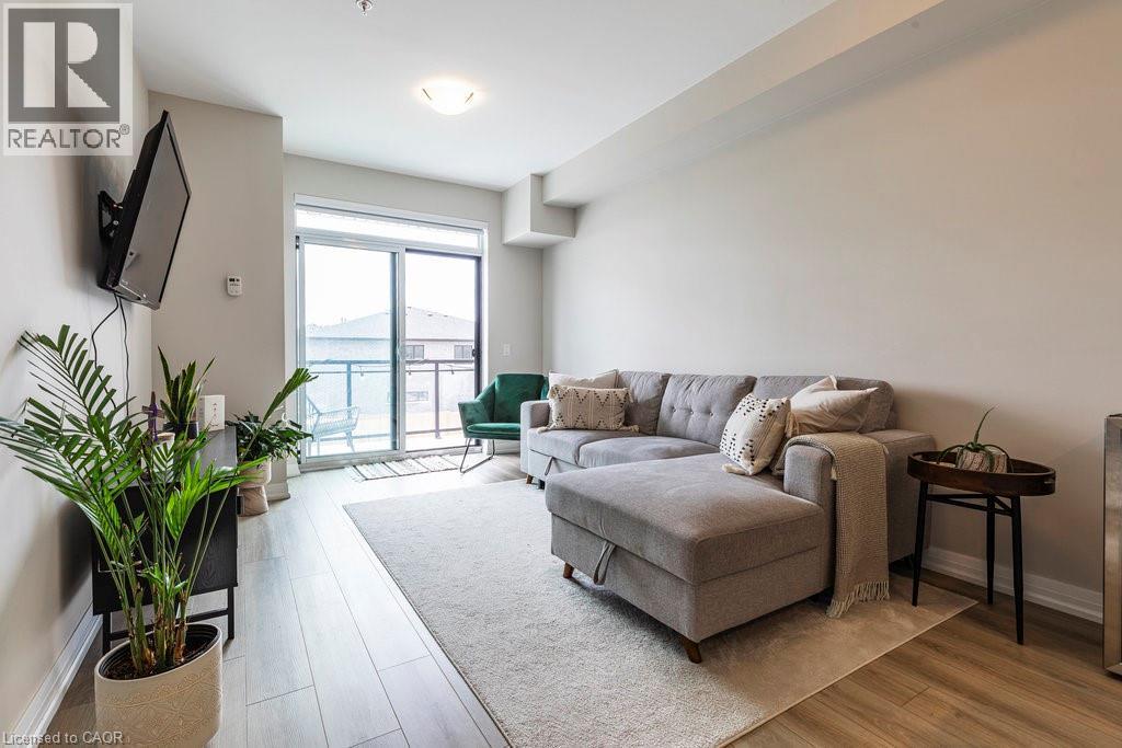 Open-concept living area featuring light wood-finish flooring, neutral wall tones, a ceiling-mounted light fixture, and floor-to-ceiling sliding glass doors opening to an outdoor balcony with a glass - 120 Springvalley Crescent Unit# 208, Hamilton, ON - Indoor Photo Showing Living Room