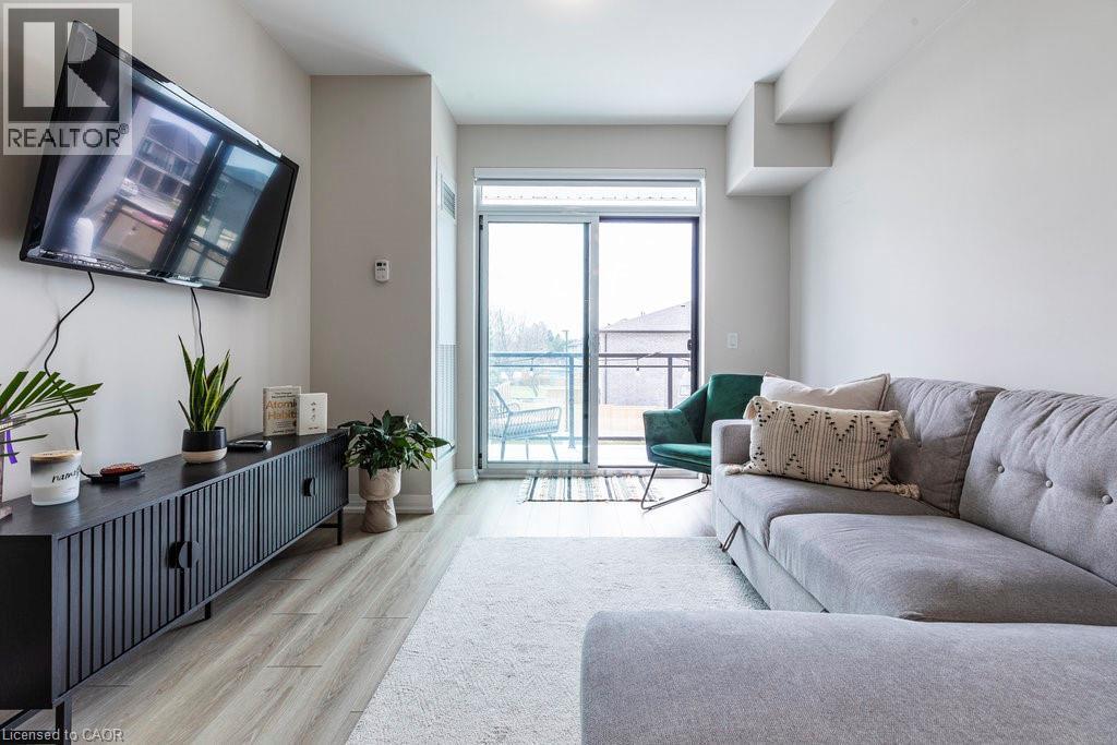 Living space featuring neutral wall tones, wood-finish flooring, a white area rug, and sliding glass doors opening to an outdoor area - 120 Springvalley Crescent Unit# 208, Hamilton, ON - Indoor Photo Showing Living Room