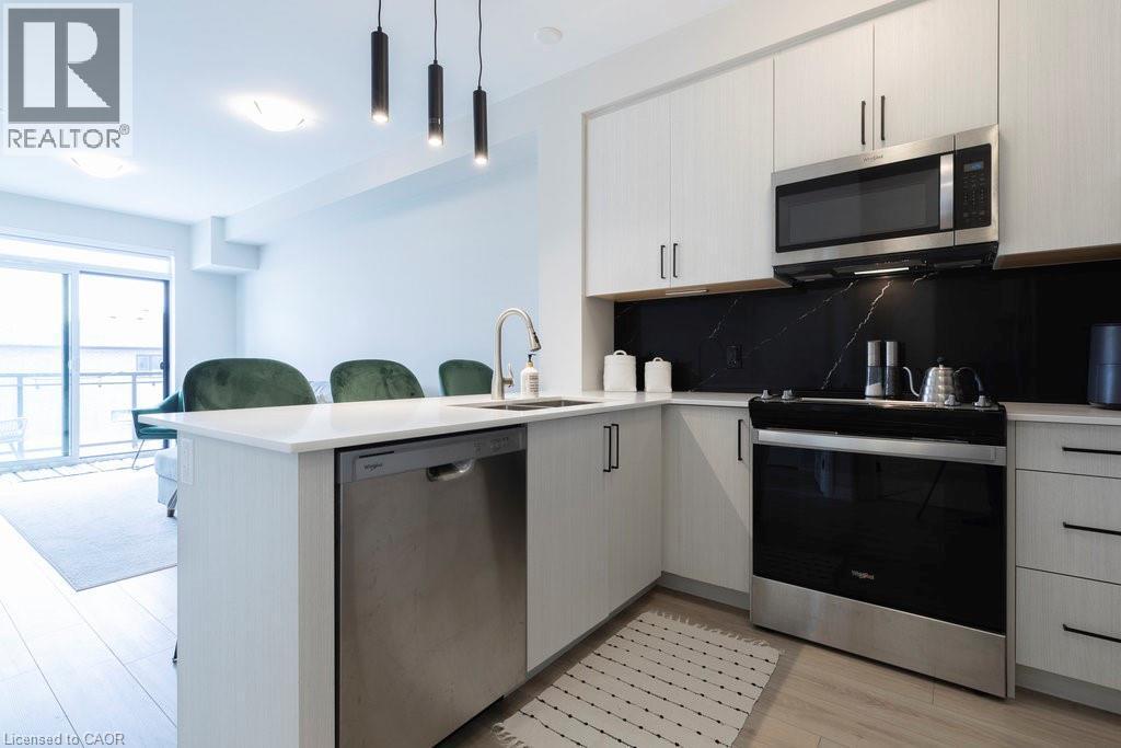 Modern kitchen featuring white cabinetry, light-toned countertops, and a striking dark backsplash - 120 Springvalley Crescent Unit# 208, Hamilton, ON - Indoor Photo Showing Kitchen With Upgraded Kitchen