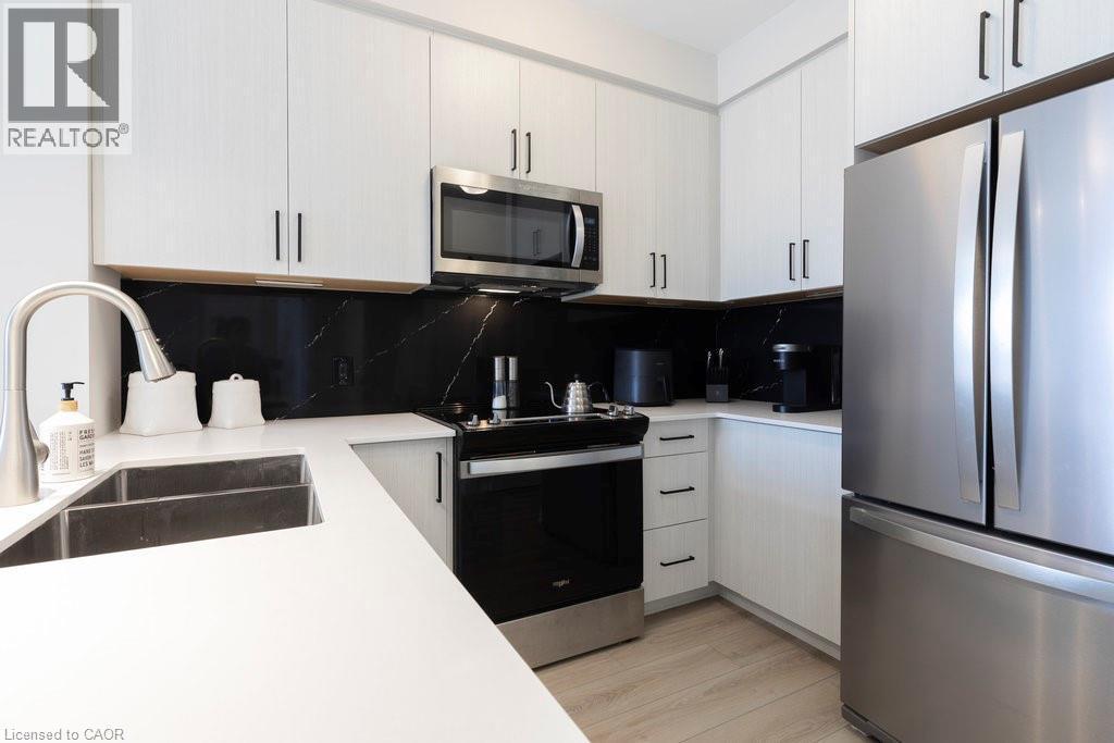 Contemporary kitchen featuring white cabinetry with dark hardware, a stainless steel appliance suite, black marble-patterned backsplash, and light wood-finish flooring - 120 Springvalley Crescent Unit# 208, Hamilton, ON - Indoor Photo Showing Kitchen With Stainless Steel Kitchen With Double Sink