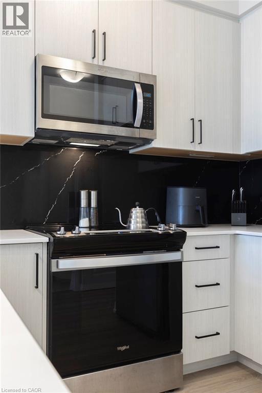 Modern kitchen with light wood-finish cabinetry, black linear pulls, and a black marble-patterned backsplash - 120 Springvalley Crescent Unit# 208, Hamilton, ON - Indoor Photo Showing Kitchen