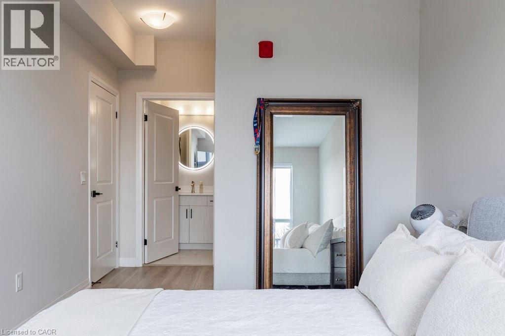 Bathroom entry featuring a vanity with a circular back-lit mirror, a wall-mounted faucet, and light wood-finish flooring - 120 Springvalley Crescent Unit# 208, Hamilton, ON - Indoor Photo Showing Bedroom