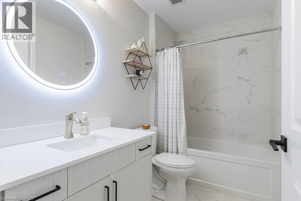 Contemporary bathroom featuring a light wood-finish vanity with black hardware, a pristine white countertop, and an integrated rectangular sink - 120 Springvalley Crescent Unit# 208, Hamilton, ON - Indoor Photo Showing Bathroom