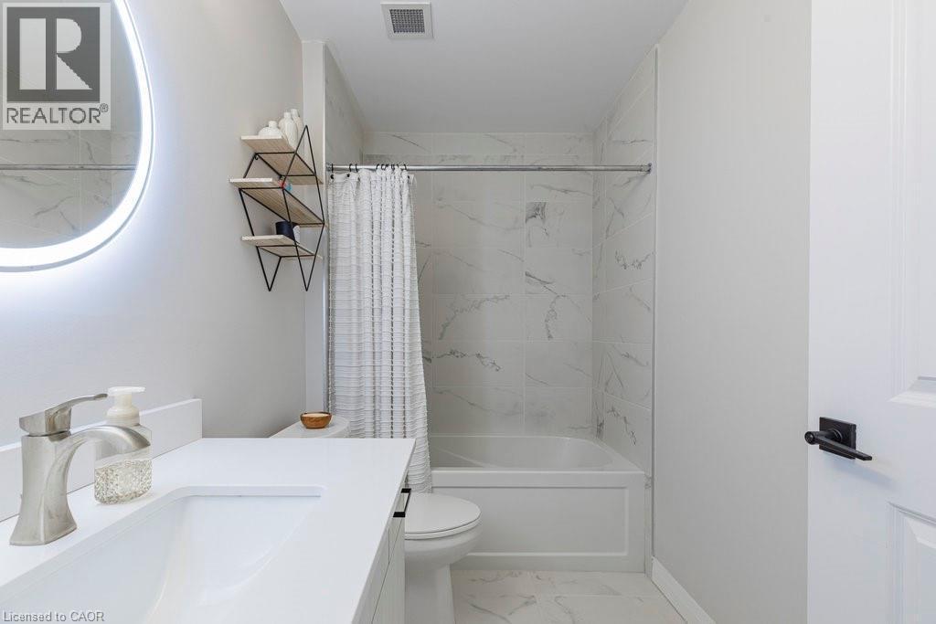 Contemporary bathroom featuring a combined tub and shower with marble-look wall tiling and a circular illuminated mirror - 120 Springvalley Crescent Unit# 208, Hamilton, ON - Indoor Photo Showing Bathroom