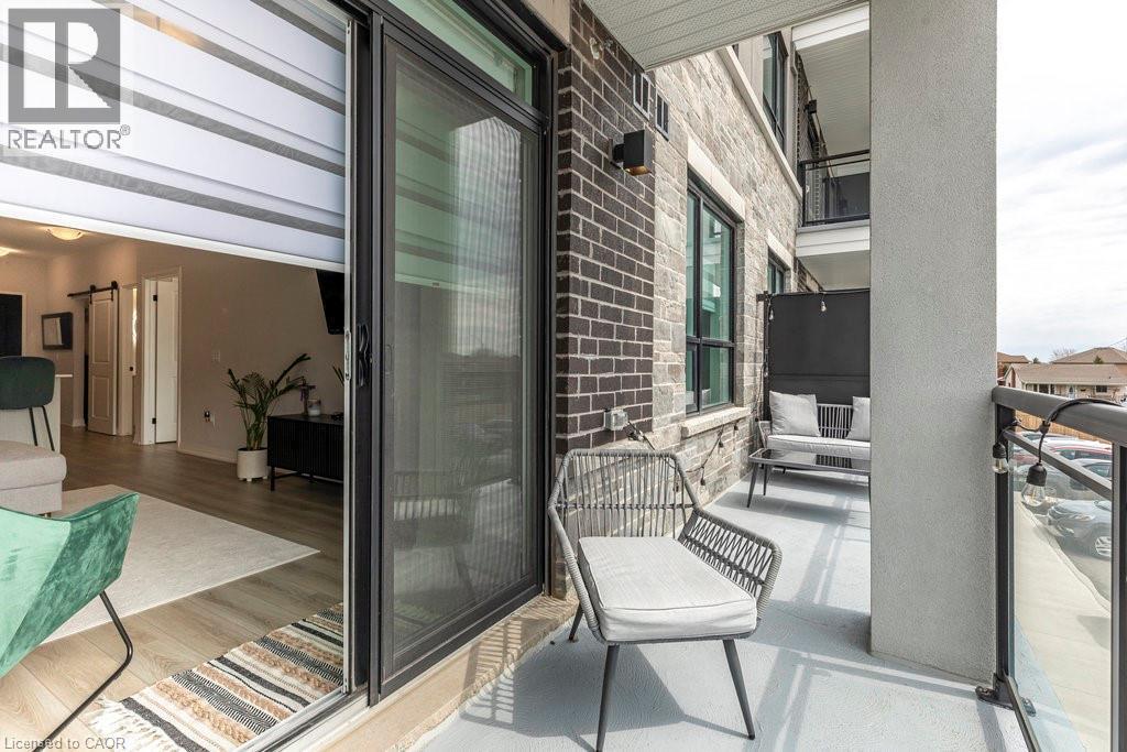 Private balcony featuring a concrete surface, black metal and glass railing, and brick and stone exterior finishes - 120 Springvalley Crescent Unit# 208, Hamilton, ON - Outdoor With Balcony With Exterior