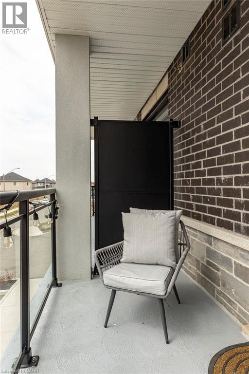 Balcony featuring a black metal and glass railing, concrete flooring, dark brick wall, and a black privacy screen - 120 Springvalley Crescent Unit# 208, Hamilton, ON - Outdoor With Balcony With Exterior
