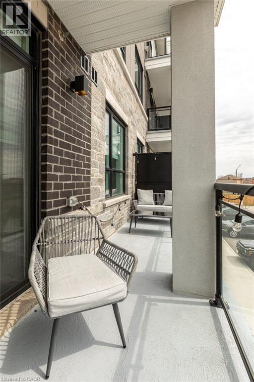 Private balcony with a concrete floor, featuring a glass panel railing and a dark brick exterior wall - 120 Springvalley Crescent Unit# 208, Hamilton, ON - Outdoor With Balcony With Exterior
