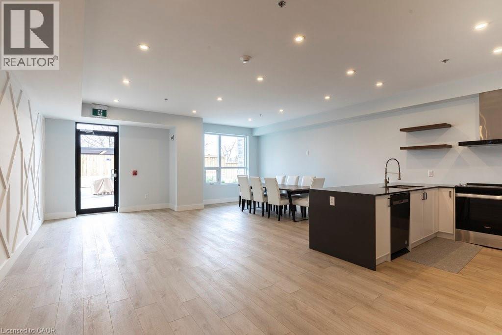 Open-concept living space featuring wood-finish flooring, recessed lighting, and a kitchen island with integrated sink - 120 Springvalley Crescent Unit# 208, Hamilton, ON - Indoor Photo Showing Kitchen With Upgraded Kitchen