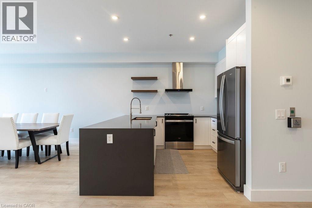 Modern open-concept kitchen featuring an oversized island with a built-in sink, stainless steel appliances, and wood-finish flooring - 120 Springvalley Crescent Unit# 208, Hamilton, ON - Indoor
