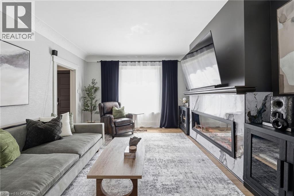 Living area featuring a linear fireplace with a marble-finish surround and a black accent wall - 361 Cumberland Avenue, Hamilton, ON - Indoor Photo Showing Living Room With Fireplace