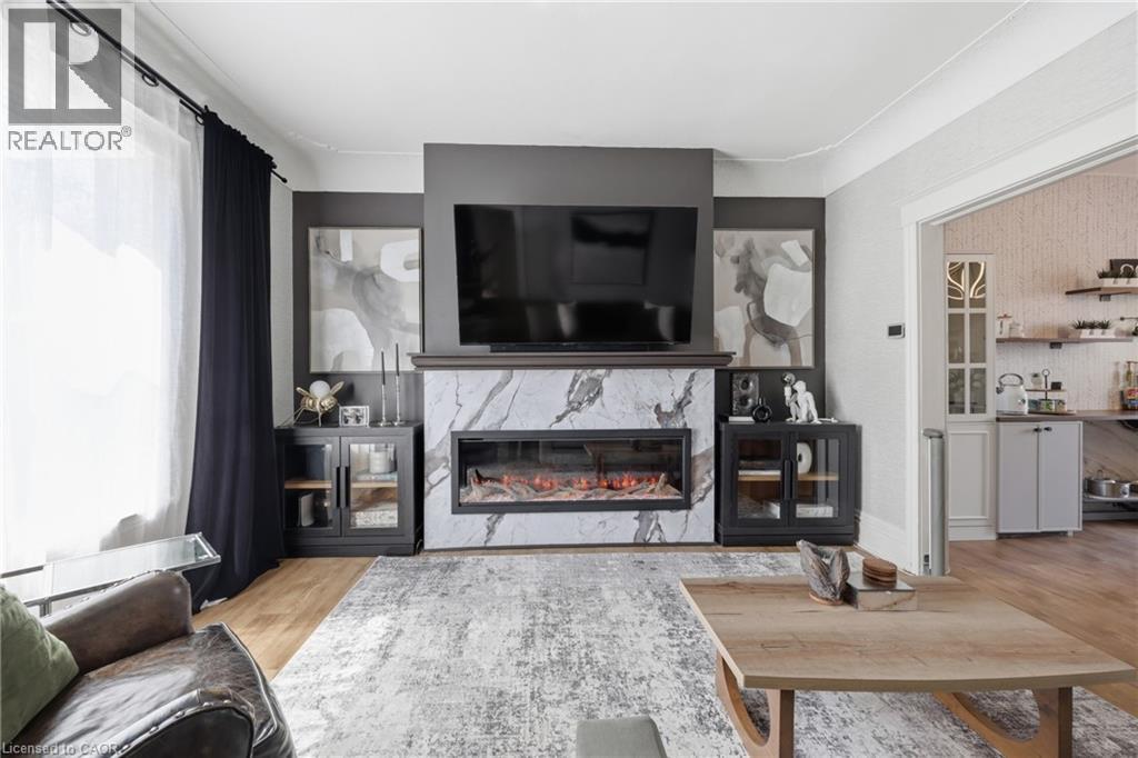 Living room featuring a large window, wood-finish flooring, and a contemporary fireplace with a marble-effect surround - 361 Cumberland Avenue, Hamilton, ON - Indoor Photo Showing Living Room With Fireplace