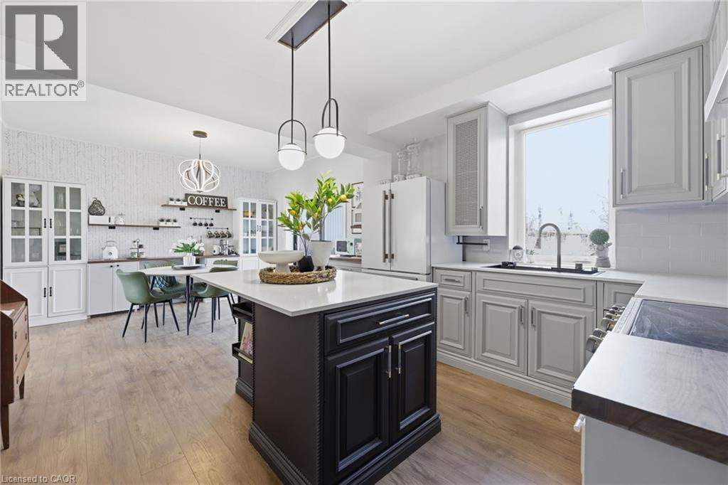 Expansive kitchen featuring a large central island with a light-toned countertop, wood-finish flooring, white subway tile backsplash, light gray cabinetry, and a built-in coffee bar with open shelving - 361 Cumberland Avenue, Hamilton, ON - Indoor Photo Showing Kitchen With Upgraded Kitchen