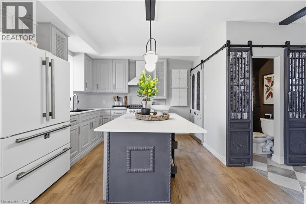Gourmet kitchen featuring a central island with a white countertop, light gray cabinetry, built-in appliances, and wood-finish flooring - 361 Cumberland Avenue, Hamilton, ON - Indoor Photo Showing Kitchen