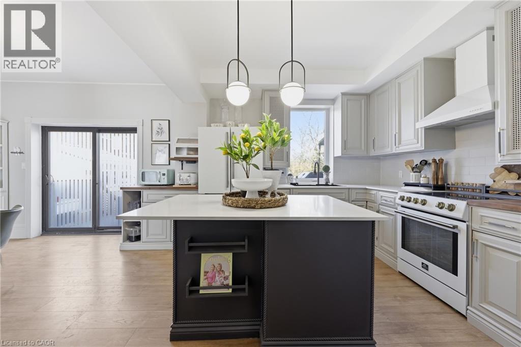 Modern kitchen featuring a central island with integrated shelving, light-toned cabinetry, light wood-finish flooring, and white appliances including a range and range hood - 361 Cumberland Avenue, Hamilton, ON - Indoor Photo Showing Kitchen With Upgraded Kitchen