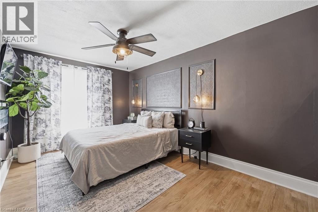 Bedroom featuring wood-finish flooring, a ceiling fan with integrated lighting, and a dark accent wall - 361 Cumberland Avenue, Hamilton, ON - Indoor Photo Showing Bedroom