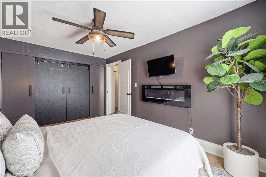 Bedroom featuring a wood-finish ceiling fan, wall-mounted electric fireplace, and dark sliding closet doors - 361 Cumberland Avenue, Hamilton, ON - Indoor Photo Showing Bedroom
