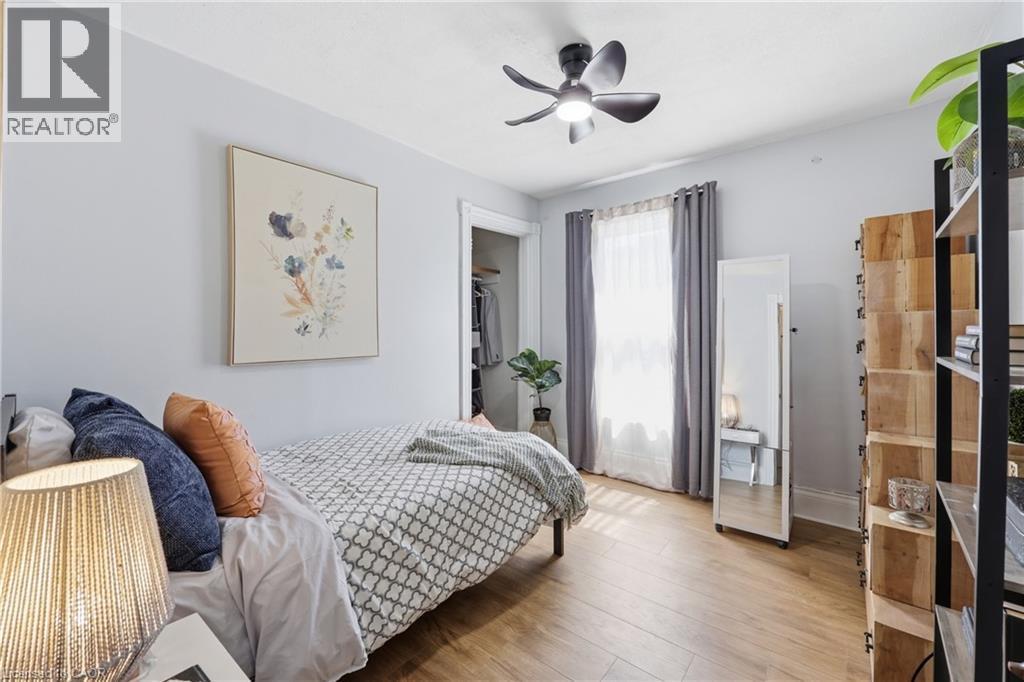Bedroom featuring wood-finish flooring, a ceiling fan with integrated lighting, and a window with drapes - 361 Cumberland Avenue, Hamilton, ON - Indoor Photo Showing Bedroom