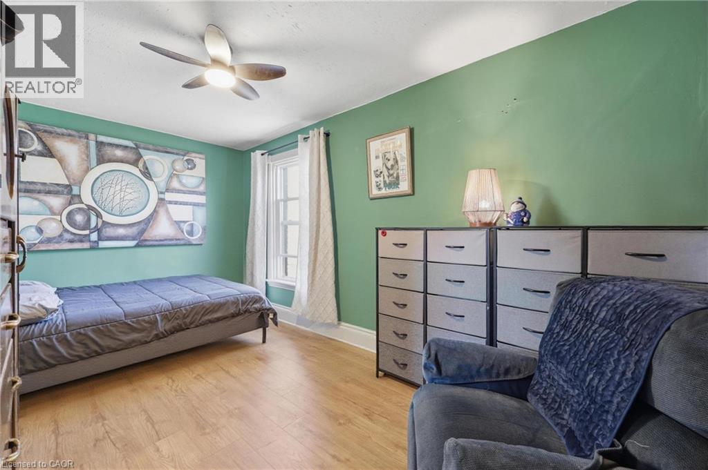Bright interior space featuring green walls, wood-finish flooring, a ceiling fan with integrated lighting, and a single window with white trim - 361 Cumberland Avenue, Hamilton, ON - Indoor Photo Showing Bedroom