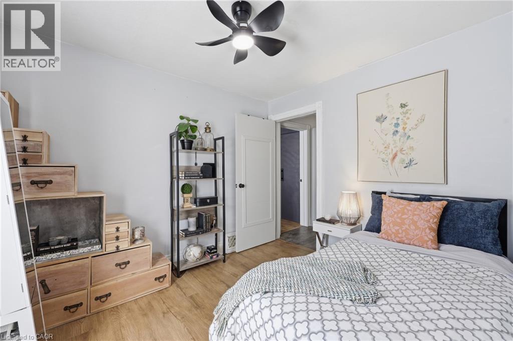 Light-filled room featuring wood-finish flooring, a modern black ceiling fan with integrated lighting, and a white paneled door - 361 Cumberland Avenue, Hamilton, ON - Indoor Photo Showing Bedroom