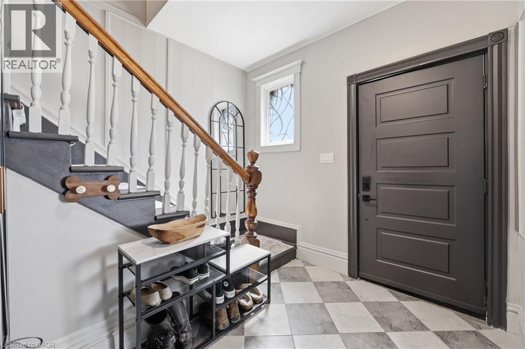 Entryway featuring a patterned tile floor, dark paneled door, traditional wooden staircase with white balusters, and transom window - 361 Cumberland Avenue, Hamilton, ON - Indoor Photo Showing Other Room