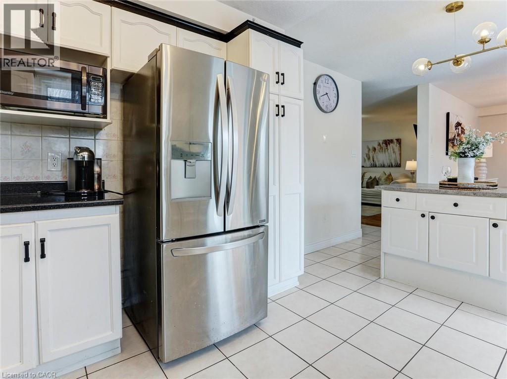 Kitchen featuring white cabinetry with black hardware, dark countertops, and a stainless steel refrigerator - 154 Deerpath Drive, Guelph, ON - Indoor Photo Showing Kitchen