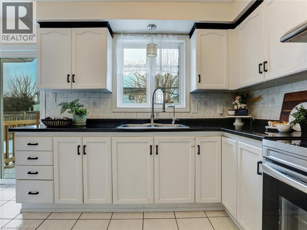 Kitchen featuring white cabinetry with black hardware, dark countertops, and a tiled backsplash - 154 Deerpath Drive, Guelph, ON - Indoor Photo Showing Kitchen With Double Sink