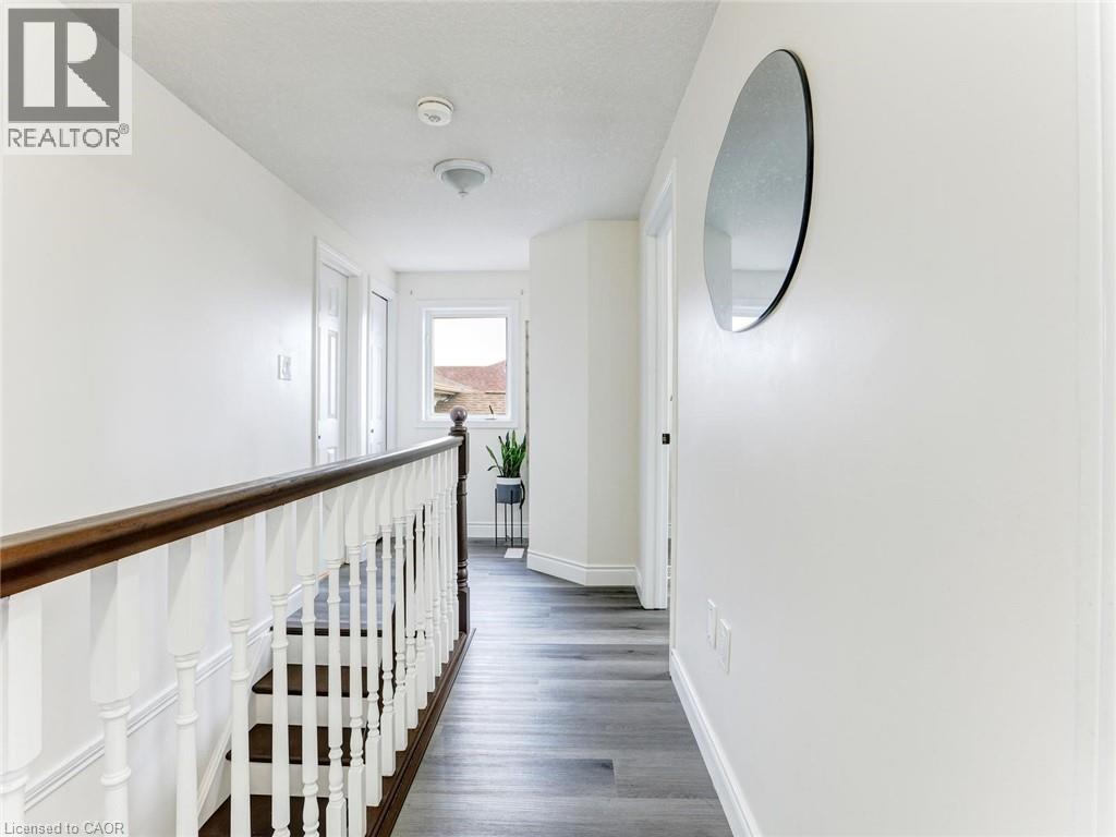 Upper-level hallway featuring wood-finish flooring, a white spindle staircase with a dark wood handrail, and a window providing natural light - 154 Deerpath Drive, Guelph, ON - Indoor Photo Showing Other Room