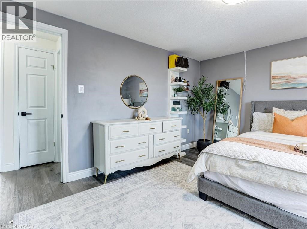Spacious interior room featuring wood-finish flooring, light gray walls, a white paneled door with black hardware, and a ceiling light fixture - 154 Deerpath Drive, Guelph, ON - Indoor Photo Showing Bedroom