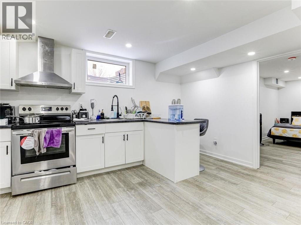 Kitchen featuring white cabinetry, stainless steel range with hood vent, black countertops, and wood-finish flooring - 154 Deerpath Drive, Guelph, ON - Indoor Photo Showing Kitchen