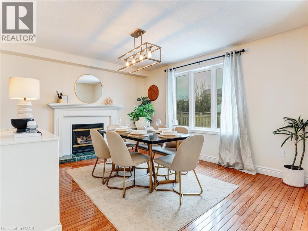 Dining area featuring wood-finish flooring, a contemporary chandelier, a white fireplace with a green tiled hearth, and a large bay window - 154 Deerpath Drive, Guelph, ON - Indoor Photo Showing Dining Room With Fireplace