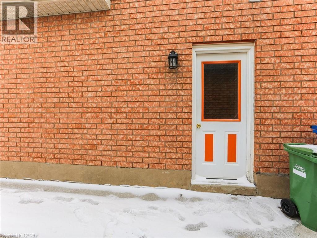 Red brick exterior featuring a white door with orange accents, an exterior wall sconce, and a concrete foundation - 154 Deerpath Drive, Guelph, ON - Outdoor
