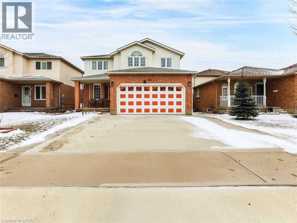 Two-story residence featuring a brick facade on the lower level and light-colored siding on the upper story, a prominent two-car garage with an orange and white paneled door, an arched window above th - 154 Deerpath Drive, Guelph, ON - Outdoor With Facade