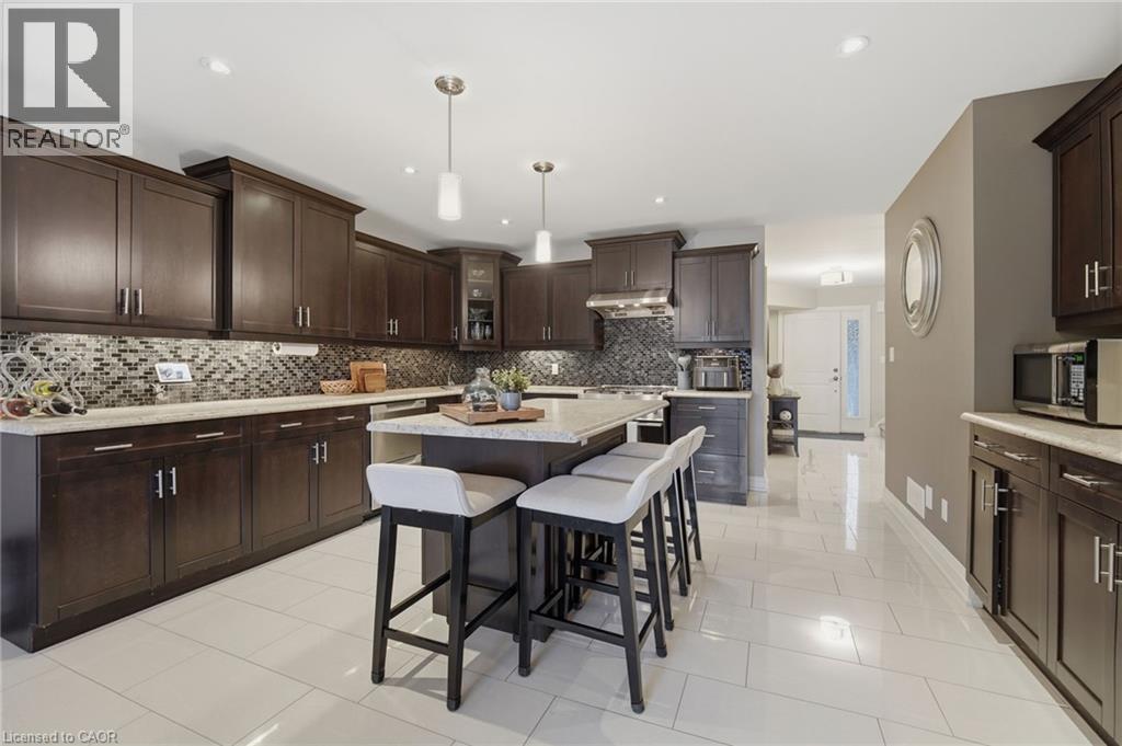 Kitchen featuring dark wood cabinetry, light-toned countertops, a mosaic tile backsplash, a central island with seating, and light-toned tile flooring - 7 Gibson Place Unit# 26, St. Catharines, ON - Indoor