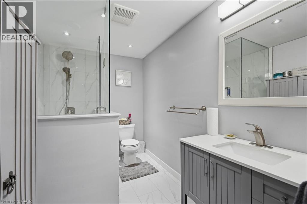 Contemporary bathroom featuring a glass-enclosed shower with white marble-look tile, a grey vanity with a white countertop and integrated sink, a large framed mirror, and recessed ceiling lighting - 7 Gibson Place Unit# 26, St. Catharines, ON - Indoor Photo Showing Bathroom