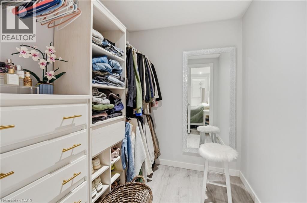 Walk-in closet featuring built-in white cabinetry, gold-tone hardware, wood-finish flooring, full-length mirror, and ample storage shelving - 7 Gibson Place Unit# 26, St. Catharines, ON - Indoor With Storage